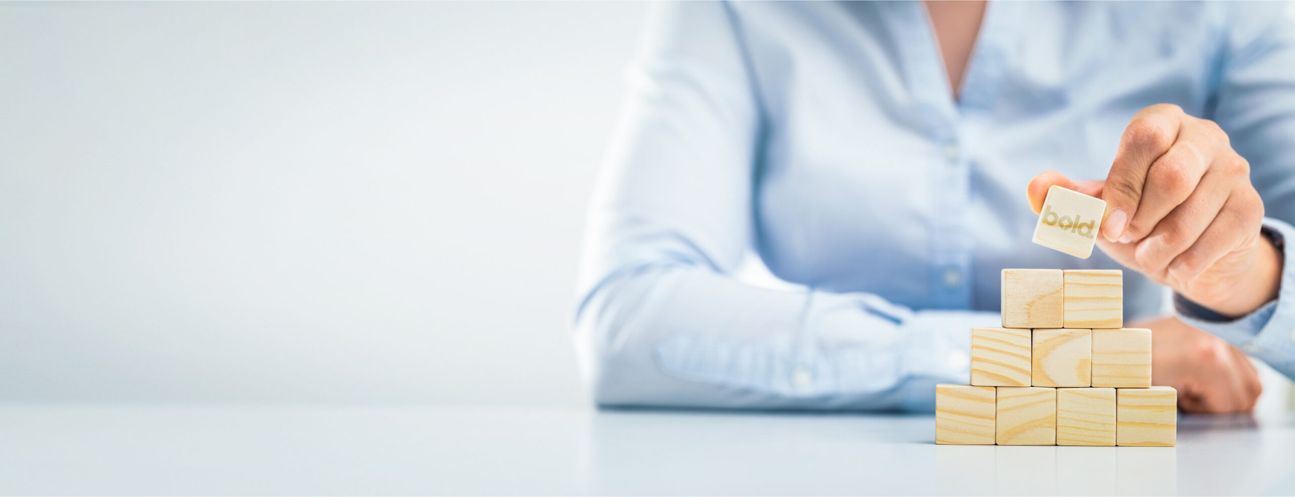 Person in a blue shirt places a wooden block labeled 'bold' on top of a stack of blocks on a white table.